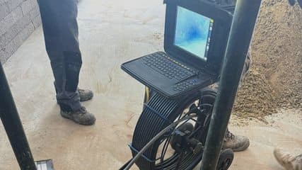 CCTV drain survey unit with the camera feed on screen, beside an open trench